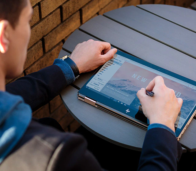 Homme utilisant un ordinateur portable à stylet numérique en mode tablette dehors sur une table - Ordinateur portable convertible puissant HP Spectre x360