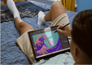 You man laying on a bed and drawing on his touch screen display, using a HP display pen