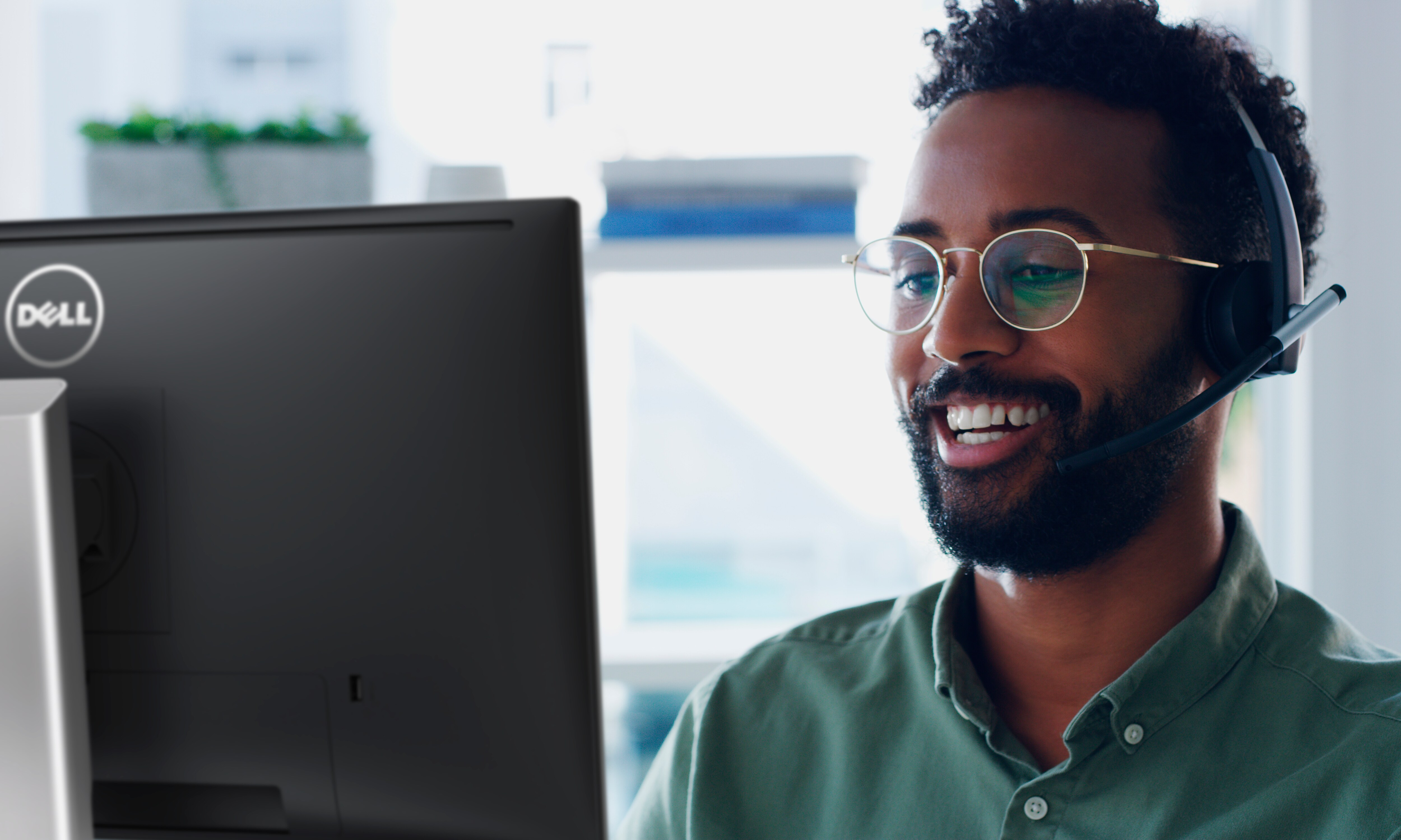 Homme souriant portant des lunettes qui utilise un écran Dell avec un casque sur la tête.