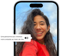 Un iPhone 15 affichant une annonce VoiceOver décrivant le contenu d'une photographie en ces termes : une personne aux cheveux noirs ondulés en train de rire